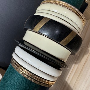 May include: A stack of bangles with a black and gold bangle on top, followed by a white bangle, a black bangle, a white bangle, and a gold bangle with a decorative pattern.