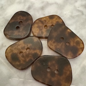 May include: Five brown and black mottled buttons with two holes each. The buttons are irregularly shaped and have a slightly translucent appearance.