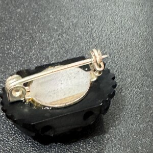 May include: A black and silver brooch with a decorative design. The brooch has a pin back and a silver tone finish.