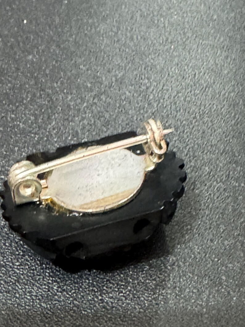 May include: A black and silver brooch with a decorative design. The brooch has a pin back and a silver tone finish.