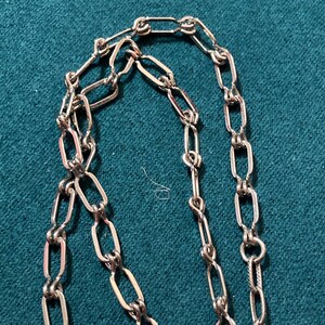 May include: A silver chain necklace with a delicate, linked design. The chain is made of small, oval-shaped links that are connected together in a repeating pattern.