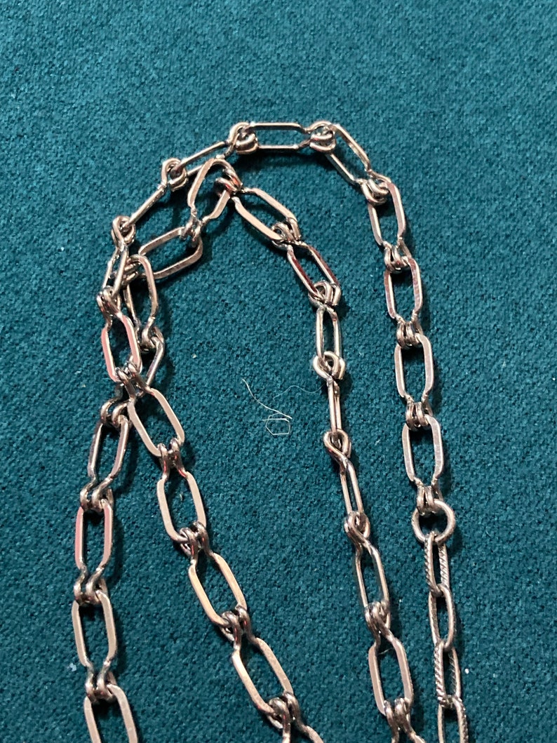 May include: A silver chain necklace with a delicate, linked design. The chain is made of small, oval-shaped links that are connected together in a repeating pattern.