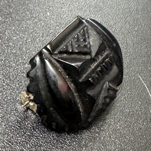 May include: A black, carved, geometric brooch with a pin on the back.