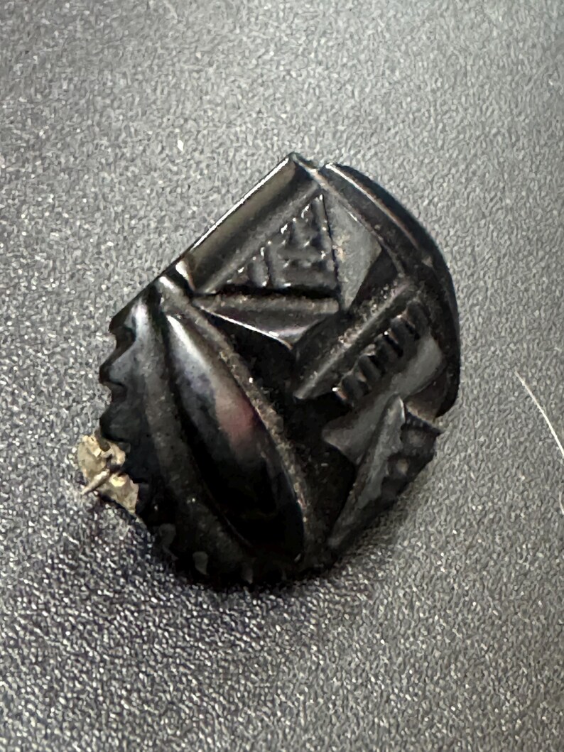 May include: A black, carved, geometric brooch with a pin on the back.