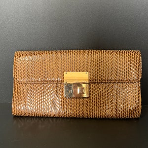 May include: A brown leather clutch with a gold lock and clasp. The clutch has a textured, snakeskin-like pattern.