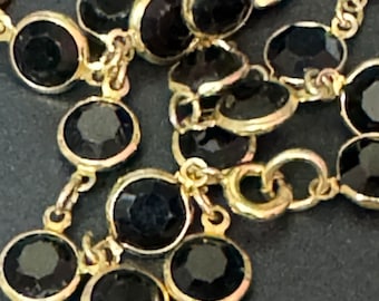 May include: A gold chain necklace with black round beads. The beads are set in gold metal.
