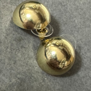Könnte beinhalten: Ein Paar goldfarbene Ohrstecker mit rundem, glattem Design. Die Ohrringe sind aus Metall und haben eine glänzende Oberfläche.