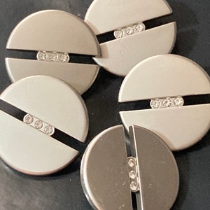 May include: Set of five silver-toned metal round buttons with a split design. Each button has three clear rhinestones in a row on the split.