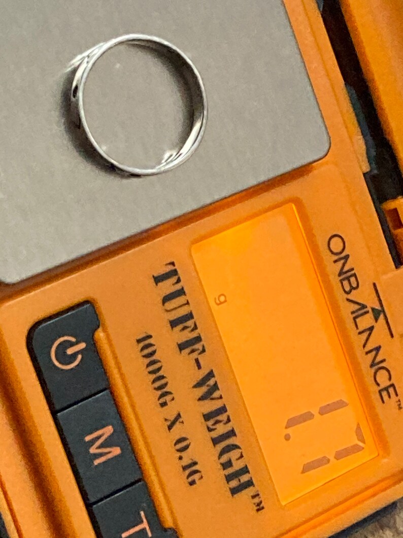 Może przedstawiać: Zbliżenie na cyfrową wagę z pomarańczową obudową. Waga wskazuje "1,1" grama. Waga jest oznaczona jako "Tuff-Weigh" i "1000g x 0,1g".