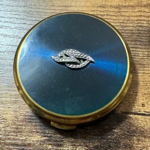 Könnte beinhalten: Ein Vintage-Kompakt-Spiegel mit einem blauen Emaille-Deckel und einem silberfarbenen, mit Strasssteinen besetzten Design. Der Kompakt hat einen Messingrand und einen Klappdeckel.