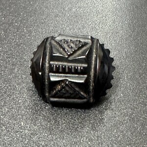 May include: A black, oval-shaped, carved glass button with intricate geometric designs.