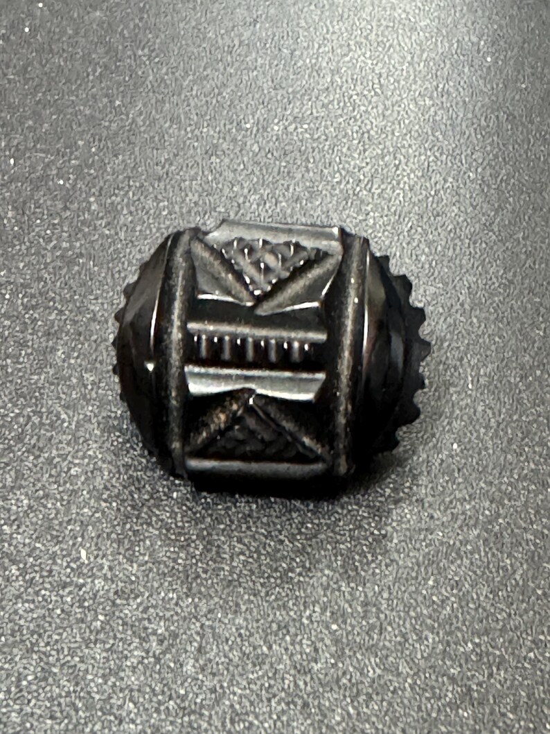 May include: A black, oval-shaped, carved glass button with intricate geometric designs.