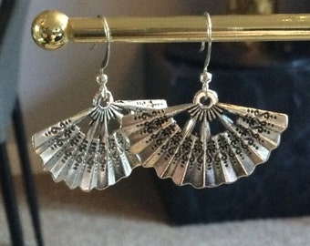 May include: A pair of silver earrings with a fan-shaped design. The earrings are hanging from a gold stand.