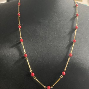 May include: A gold chain necklace with red beads. The necklace is on a black mannequin.