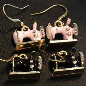 Puede incluir: Un par de pendientes de tono dorado con un dise&ntilde;o de m&aacute;quina de coser en miniatura. Un par es rosa con pedrer&iacute;a y el otro par es negro con pedrer&iacute;a.