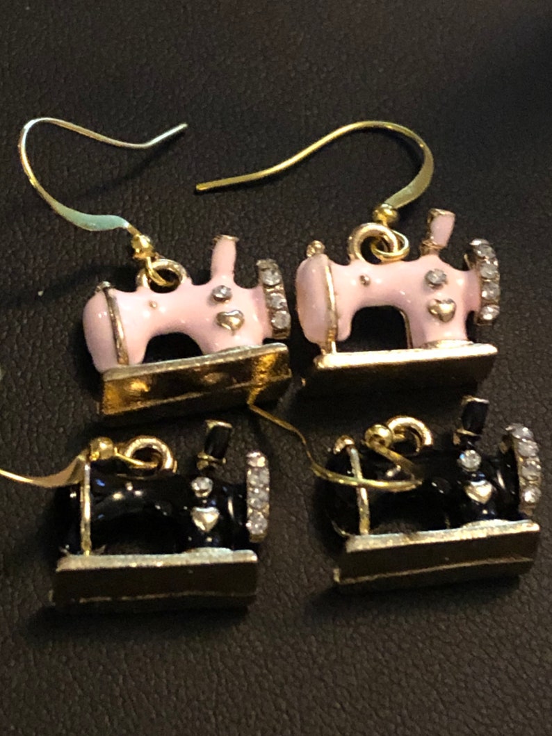 Puede incluir: Un par de pendientes de tono dorado con un dise&ntilde;o de m&aacute;quina de coser en miniatura. Un par es rosa con pedrer&iacute;a y el otro par es negro con pedrer&iacute;a.
