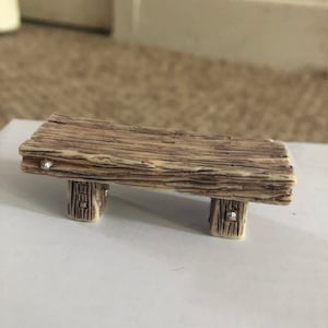 Peut inclure: Un petit banc en bois avec une finition rustique brune et des accents métalliques argentés. Le banc a un design simple avec quatre pieds et un dessus plat.
