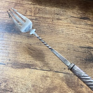 May include: A silver fork with a twisted handle. The fork has three tines and a decorative design on the handle.