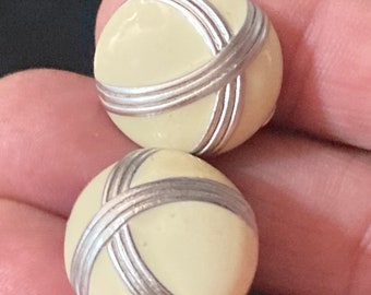 May include: Two cream-colored round buttons with silver-colored criss-cross designs.