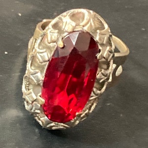 May include: A silver ring featuring an oval red gemstone set within an intricate filigree design.