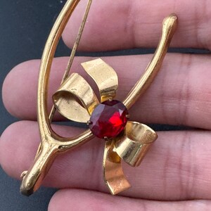 May include: Gold-tone horseshoe brooch with a red rhinestone bow. The horseshoe is open at the top and the bow is centered on the horseshoe.