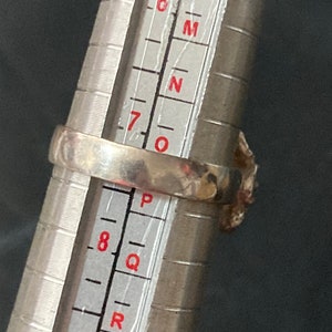 May include: A silver ring with a textured band, measured on a ring sizer. The ring size is between 7 and 8.