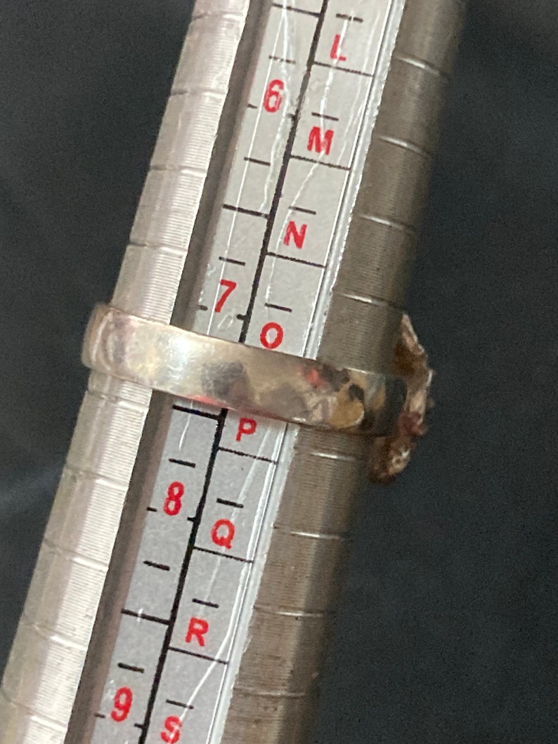 May include: A silver ring with a textured band, measured on a ring sizer. The ring size is between 7 and 8.