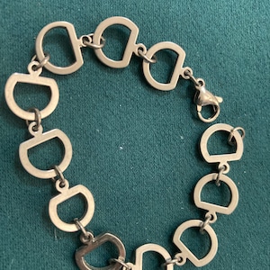 May include: A silver bracelet with a chain made of interlocking D-shaped links. The bracelet has a lobster claw clasp.