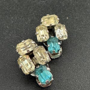 May include: Vintage silver-tone clip-on earrings. Each earring features a cluster of rectangular, faceted crystals in shades of yellow and aqua blue. The crystals are set in a silver-tone metal setting.