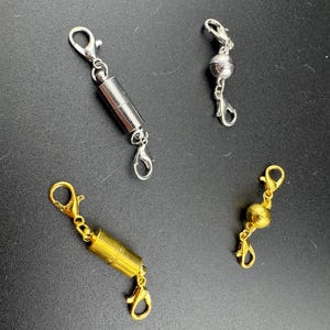 May include: Three magnetic clasps for necklaces or bracelets. One is silver with a round magnetic ball, one is gold with a round magnetic ball, and one is silver with a cylindrical magnetic piece.