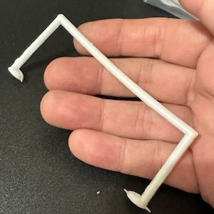 May include: White plastic support for a shelf or display stand. The support has two curved arms and a flat base.