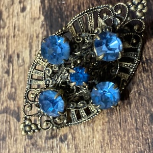 May include: A vintage brooch with a filigree design and four blue glass stones.