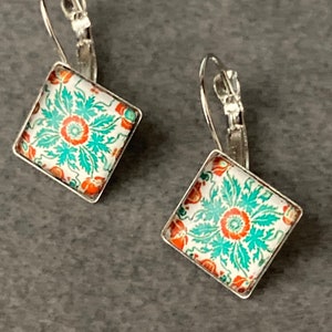 May include: A pair of silver dangle earrings with square turquoise, white and orange floral patterned glass tiles.