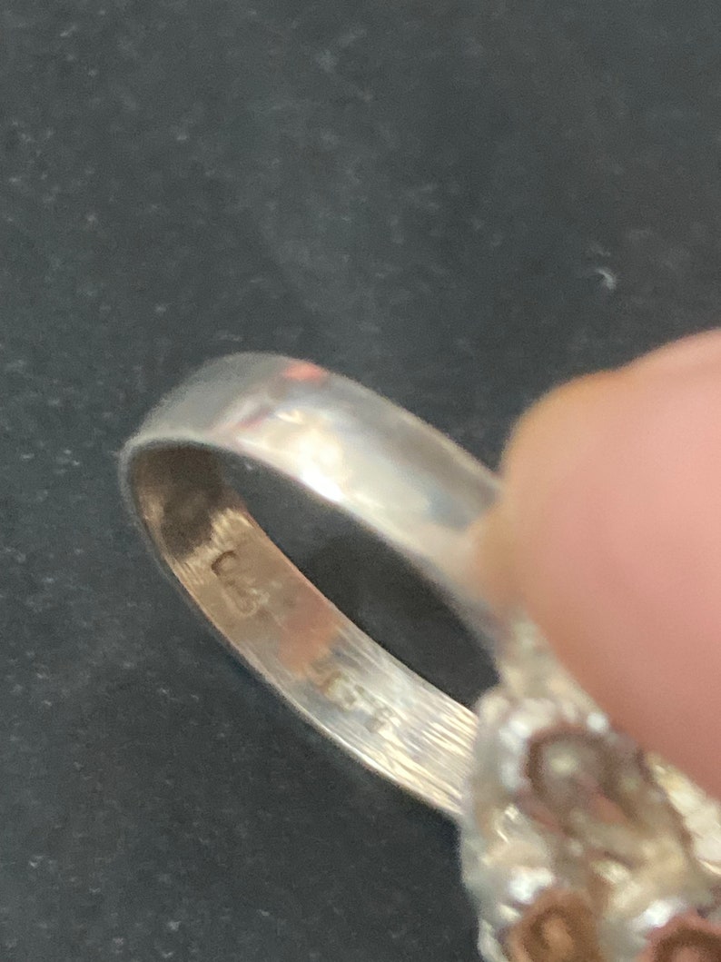 May include: Close-up of the inside of a silver ring with a floral design. The ring is marked with the number "925" on the inside band.
