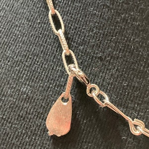 May include: Close-up of a silver chain necklace with a teardrop-shaped clasp.