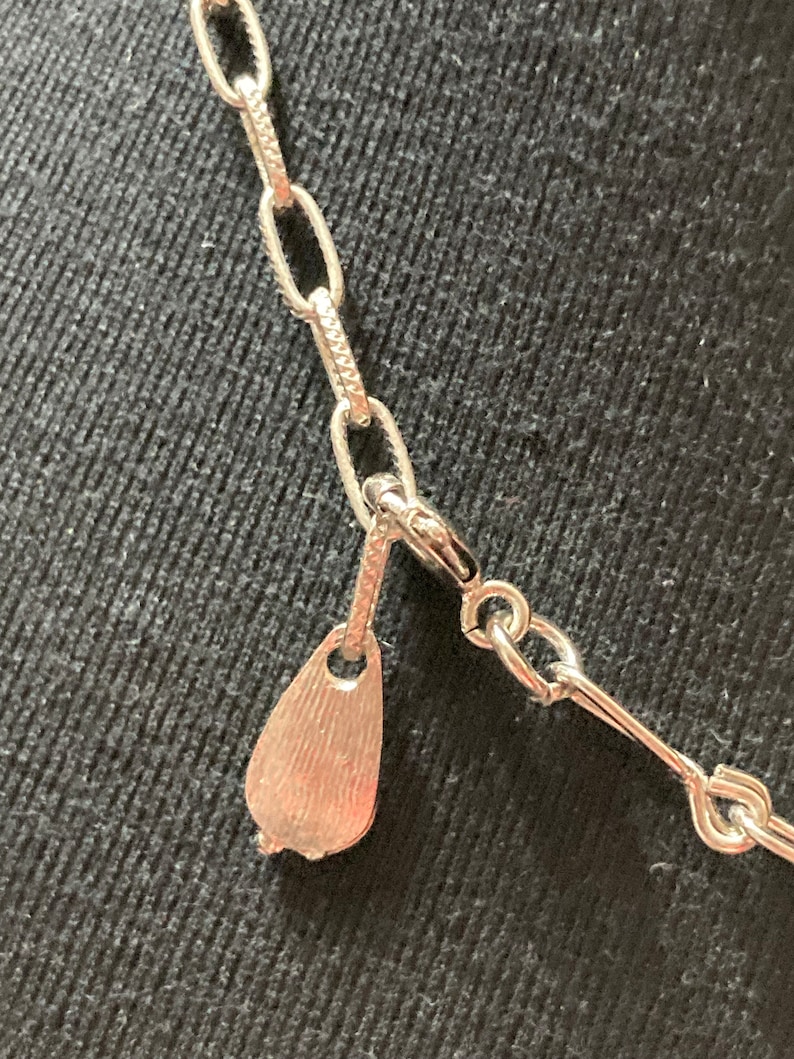 May include: Close-up of a silver chain necklace with a teardrop-shaped clasp.