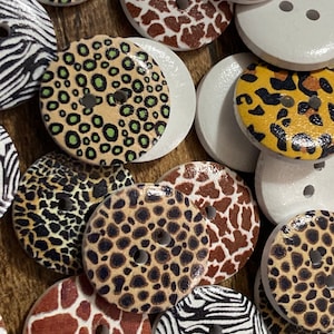 May include: Assortment of wooden buttons with various animal print designs, including zebra, leopard, giraffe, and cheetah. The buttons are round and have two holes.