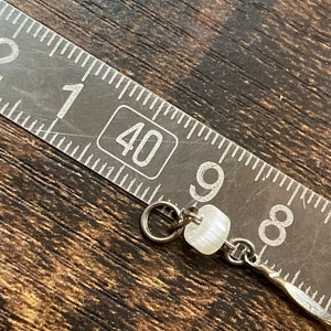 Pu&ograve; includere: Primo piano di una perla bianca su una catena d'argento. La perla ha un diametro di circa 1,2 cm e una superficie leggermente strutturata. La catena &egrave; larga circa 0,3 cm e ha un design semplice e collegato.