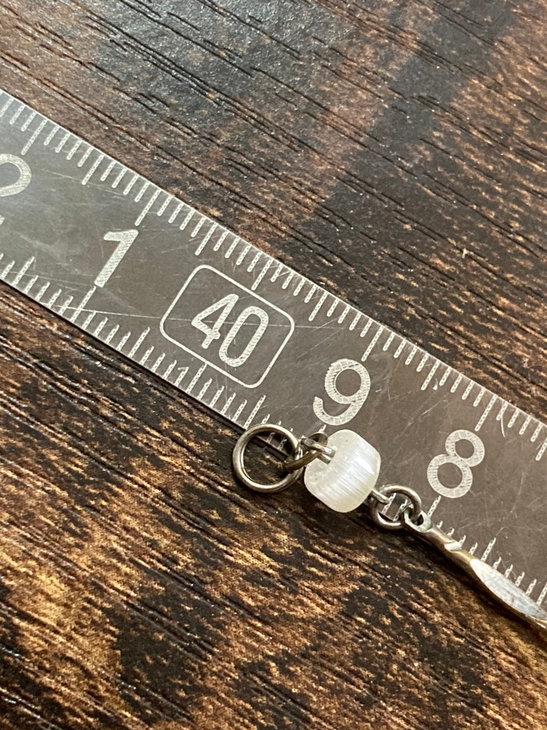 Pu&ograve; includere: Primo piano di una perla bianca su una catena d'argento. La perla ha un diametro di circa 1,2 cm e una superficie leggermente strutturata. La catena &egrave; larga circa 0,3 cm e ha un design semplice e collegato.