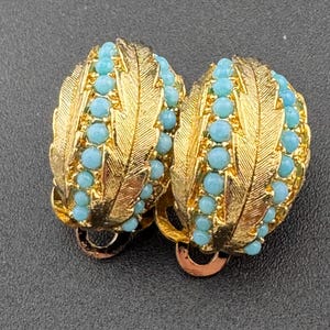May include: A pair of gold tone clip-on earrings with blue turquoise stones set in a leaf design.