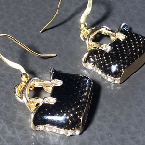 Puede incluir: Un par de pendientes colgantes de oro con dijes de bolso negro. Los bolsos est&aacute;n decorados con diamantes de imitaci&oacute;n.