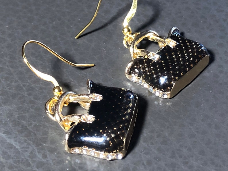 Puede incluir: Un par de pendientes colgantes de oro con dijes de bolso negro. Los bolsos est&aacute;n decorados con diamantes de imitaci&oacute;n.