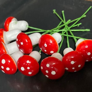 May include: A bunch of ten red and white mushroom shaped ornaments with green stems. The mushrooms are approximately 2.5 cm in diameter.