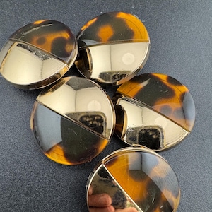 May include: Five round, brown and gold buttons with a tortoiseshell pattern. The buttons are half brown and half gold.