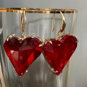 May include: A pair of gold heart-shaped earrings with red crystal accents.