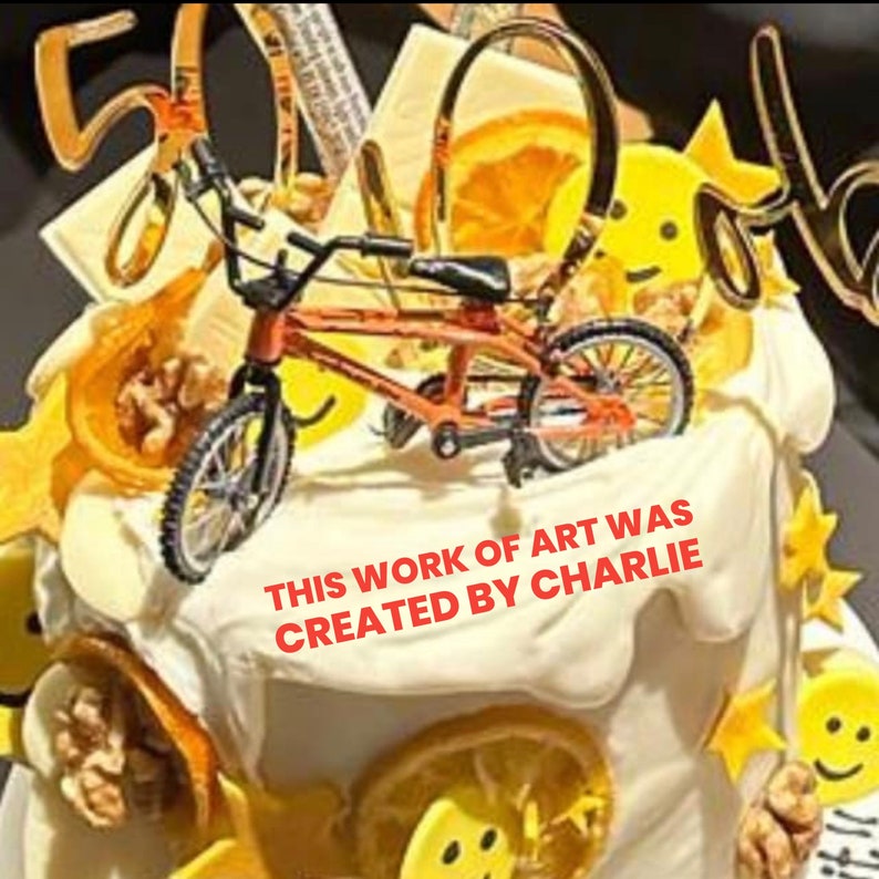 Op de afbeelding: Een versierde taart met een kleine oranje BMX-fiets erop. De taart is versierd met sinaasappelschijfjes, gele stervormige decoraties en de tekst "THIS WORK OF ART WAS CREATED BY CHARLIE".