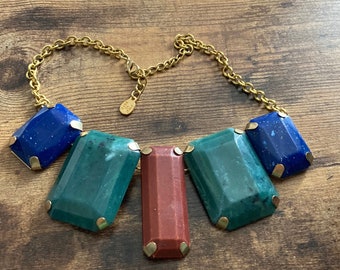 May include: A gold chain necklace with five large, faceted gemstone pendants. The pendants are in shades of blue, green, and red.