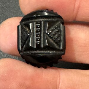 May include: A black, carved, rectangular button with a geometric design.