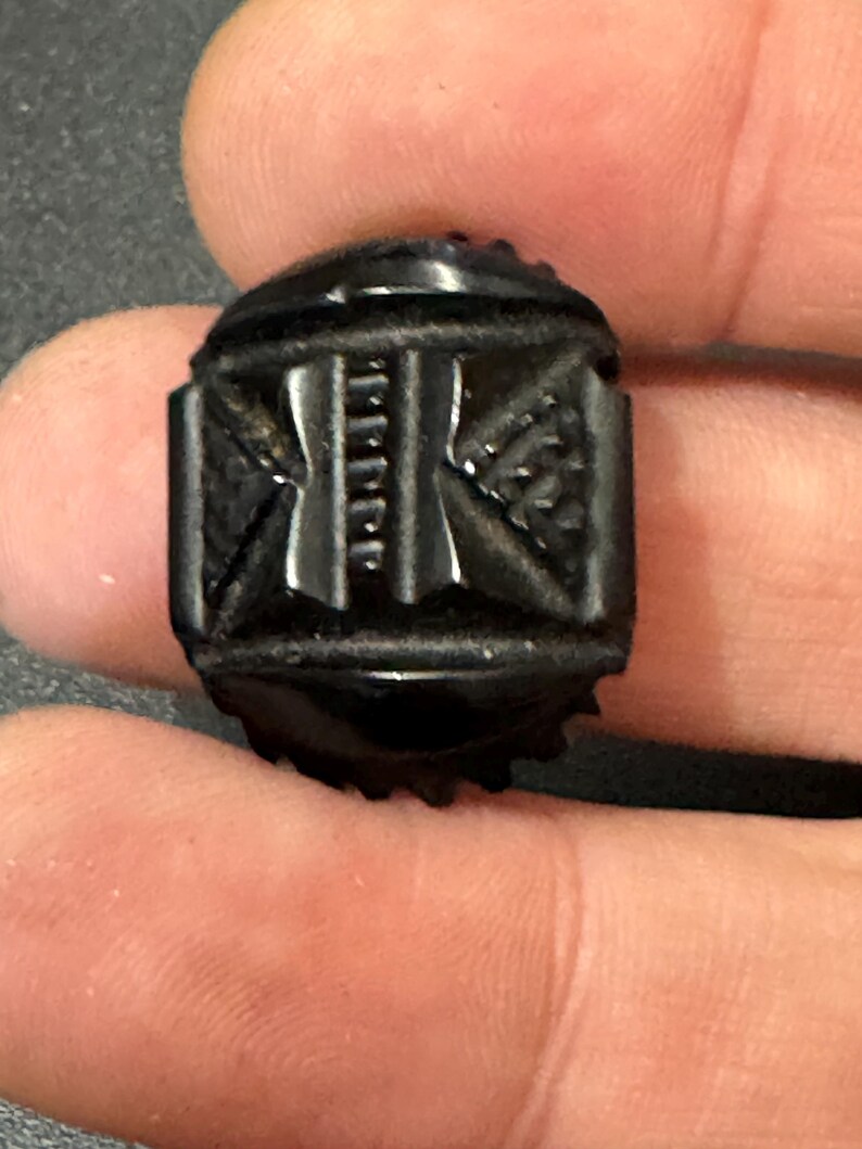 May include: A black, carved, rectangular button with a geometric design.