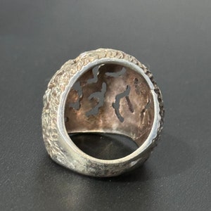 May include: A silver ring with an intricate, openwork design. The ring is made of a textured metal and has a wide band.